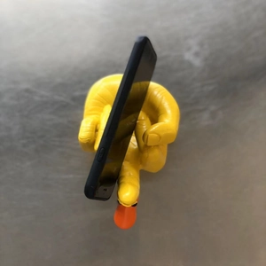 Close-up of funny yellow duck hand sculpture holding a smartphone on a desktop surface