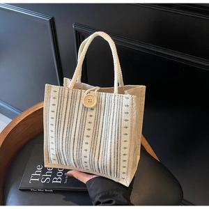 Close-up of beige linen tote bag with vertical stripes and a natural wooden button closure