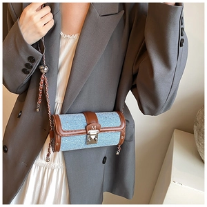Detail of blue denim barrel bag with brown leather trim and silver metal chain strap