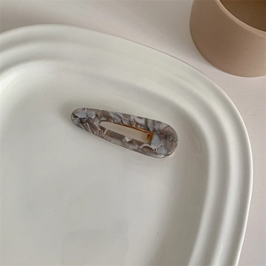 Detail of elegant acetate duckbill hair clip with marble pattern on ceramic tray