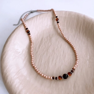Detailed view of beaded tiger eye stone and pink pearl necklace on ceramic tray