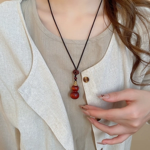 Close-up of wood gourd pendant with black cord on model in Zen style necklace