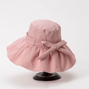 Detail of pink wide brim sun hat with ribbon bow and textured fabric on wooden stand