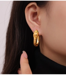 Close-up of a gold snake-shaped hoop earring with green gemstone eyes on a model