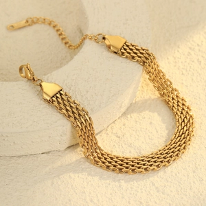 Primer plano de pulsera de malla dorada con dije de corazón sobre base de piedra
