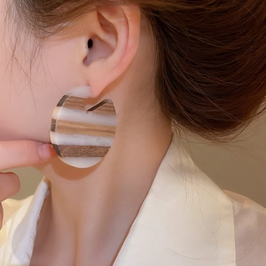 Close-up of C-shaped wood and resin earrings on model with striped pattern detail