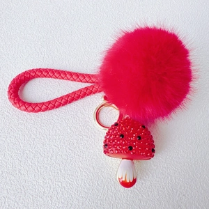 Close-up of red fluffy pom pom keychain with rhinestone mushroom charm and woven strap