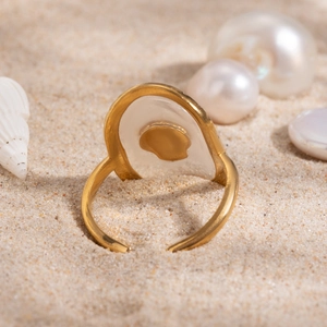 Detail of 18k gold open ring with white shell inlay set on sand with pearls