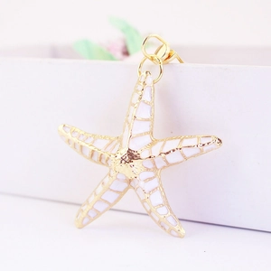 Macro shot of white enamel starfish keychain with golden metal border on white box