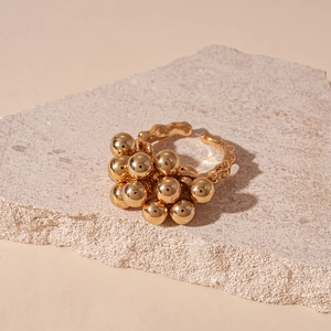 Detail view of gold clustered sphere ring displayed on a minimalist stone surface