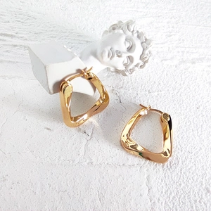 Artistic detail of gold geometric twisted triangle earrings on a white plaster background