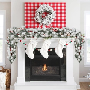 Detail of 180cm flocked Christmas garland with red berries draped on a cozy fireplace