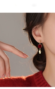 Close-up of red flocked round tassel earrings with gold sequins on a female model