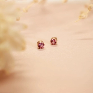 Macro shot of rose gold stud earrings with round purple gemstones and faceted sparkles