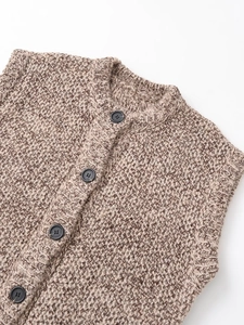 Detail of chunky knit brown vest featuring a ribbed crew neck and dark four-hole buttons