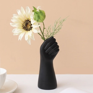 Jarrón moderno de resina negra en forma de puño con girasol sobre mesa blanca