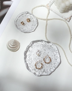 Flat lay of gold earrings and pearl pendant on irregular cracked glass display trays