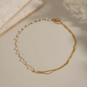 Close-up of elegant double-layered gold necklace with pearl and snake chain detail