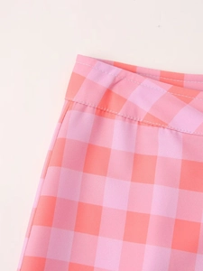 Close-up of pink and coral plaid fabric texture and stitching details of the casual pants