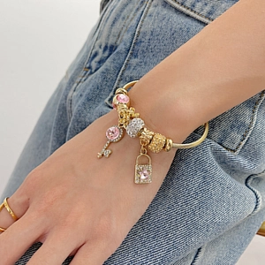 Detail of beaded gold chain bracelet with pink gemstone key and star charms on denim