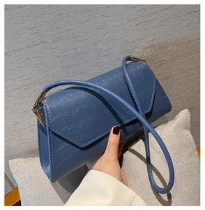 Dettaglio borsa a tracolla blu con motivo a coccodrillo e design a patta triangolare