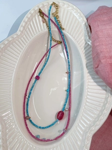 Detail of turquoise and pink beaded layered necklace on white ceramic plate