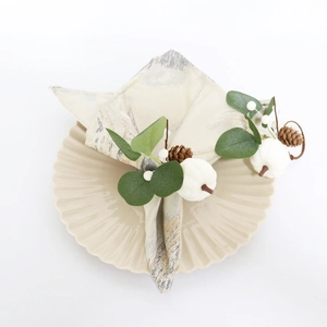 Detail of white pumpkin napkin ring with faux greenery and pine cone on dinner plate