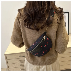 Close-up of black nylon crossbody bag with red cherry prints and leather logo detail