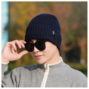 Detail of navy blue ribbed knit beanie with side logo label worn in outdoor setting