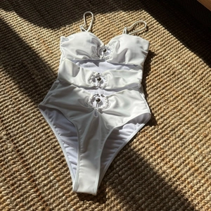 Détail du maillot de bain blanc découpé avec des anneaux en métal argenté sur fond tissé