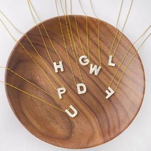 Vue détaillée de colliers dorés avec pendentifs alphabet en nacre sur un plateau en bois