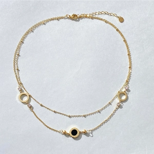 Detail of gold double-layered necklace featuring Roman numerals and a black circular pendant