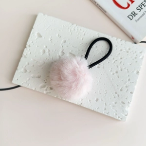 Close-up of pink fluffy pompom hair tie on a white stone background for a sweet style