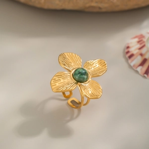 Détail d'une bague fleur dorée vintage avec pierre verte sur fond de pierre élégant