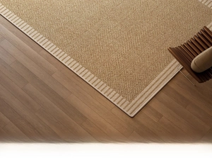 Detail of woven linen carpet with herringbone pattern and striped border on wood floor