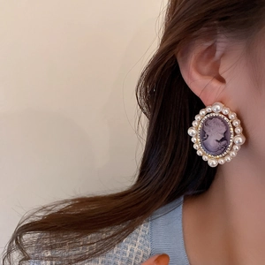 Close-up of vintage oval earring with purple cameo, pearls and sparkling crystals