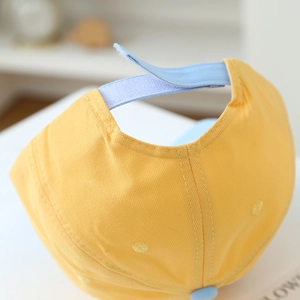 Dettaglio del cinturino in velcro blu e del tessuto in cotone sul berretto giallo
