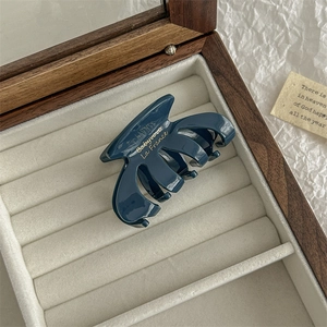 Detailed close-up of dark blue glossy hair claw clip inside a wooden jewelry box
