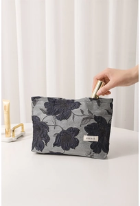Detail of hand putting cosmetics into blue floral jacquard makeup bag with label