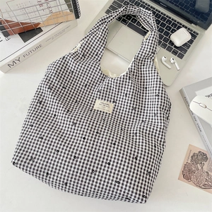 Detail of plaid tote bag with floral embroidery and branded tag on white office desk