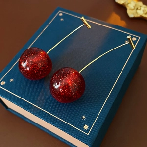 Detail view of cherry earrings with sparkling red resin fruit and golden metal stems