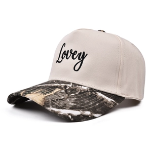 Detail of five-panel cap with Lovey embroidery and camouflage brim on beige canvas