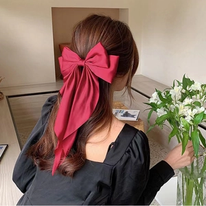 Detail of a large red satin bow hair clip on model's hair showing elegant drape and silk texture