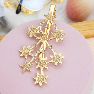 Close-up of golden star-shaped hair clip with inlaid rhinestones on a pink display