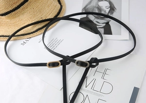 Detail of two black slim leather belts with gold and silver oval metal buckles