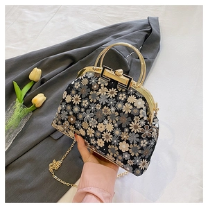 Detail of floral embroidery on black shell bag with golden metal frame and chain strap