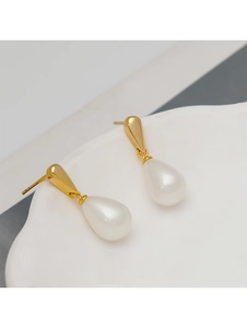 Close-up of golden teardrop pearl earrings on a minimalist white display tray