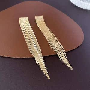 Close-up of gold metal tassel earrings featuring snake chains on leather texture