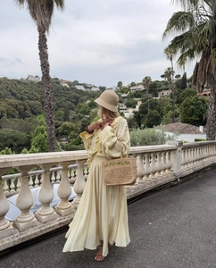 Dettaglio di un abito lungo giallo con volant, cappello e borsa di paglia in balcone