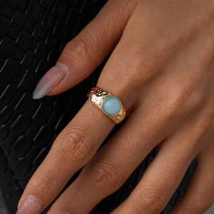 Détail macro d'une bague dorée martelée avec pierre précieuse bleu clair portée